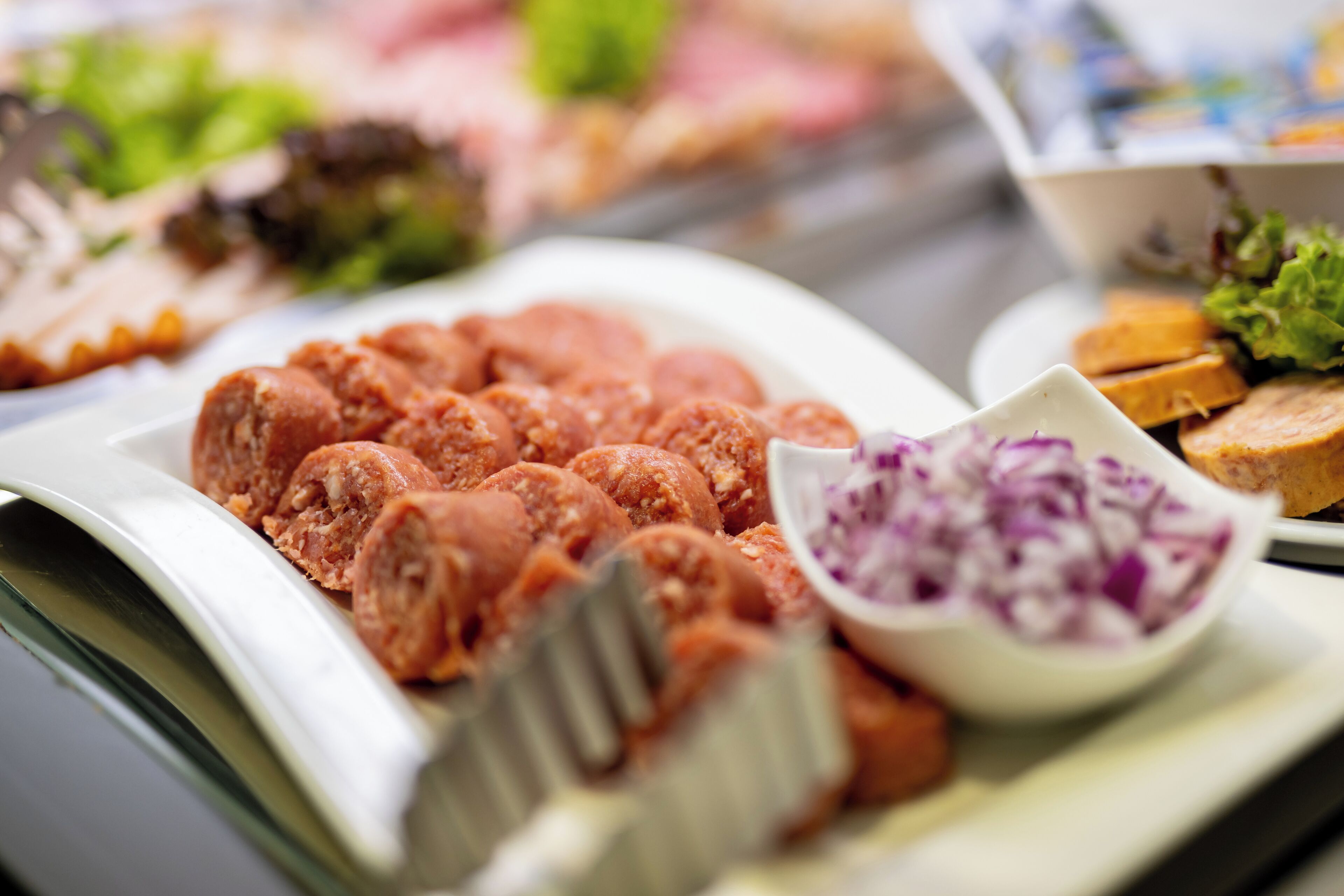 Buffet com diversos pratos, incluindo carne fatiada, uma tigela de cebolas vermelhas e alguns vegetais.