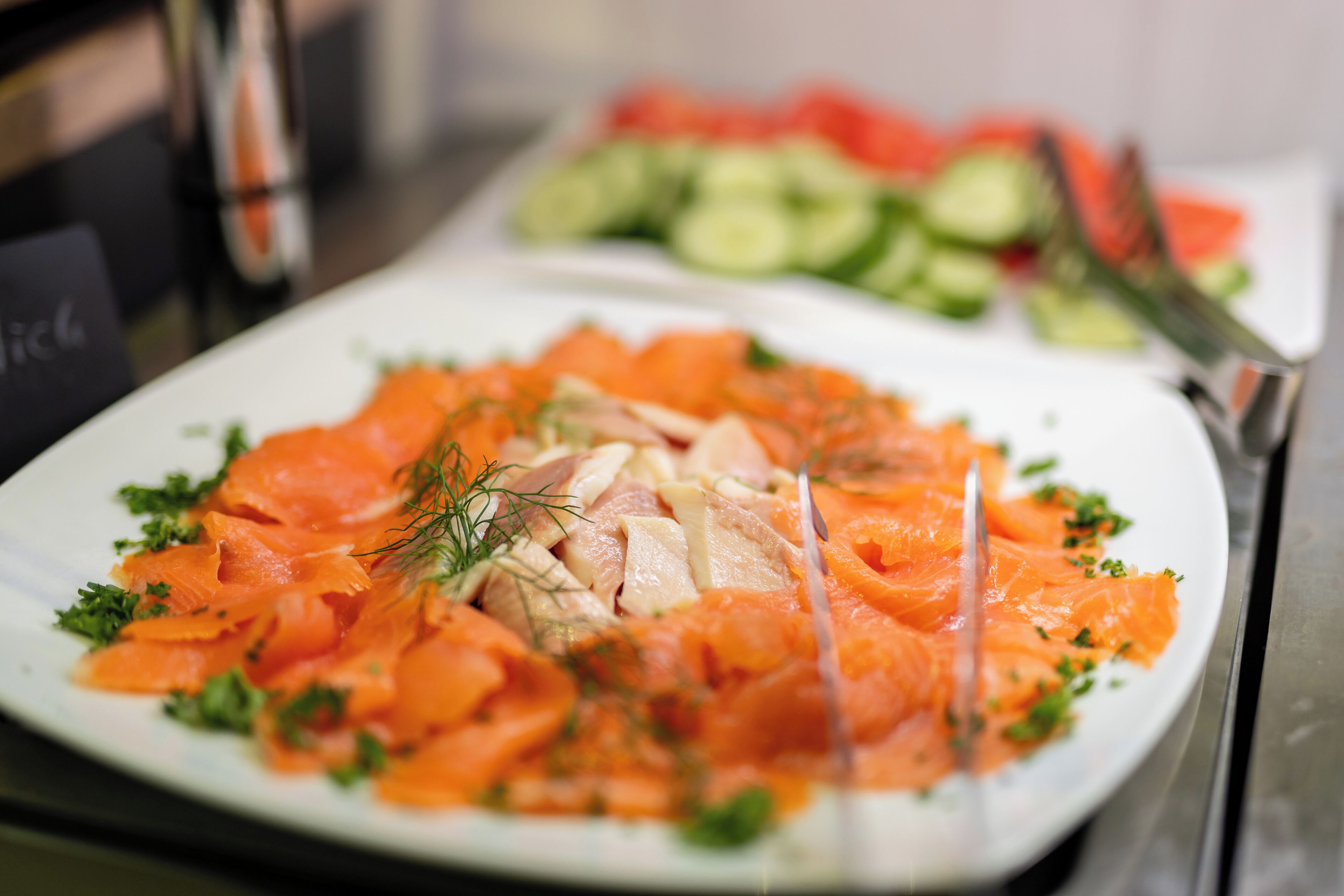 Une assiette de saumon fumé, garnie d’aneth et de persil, avec une fourchette à côté.