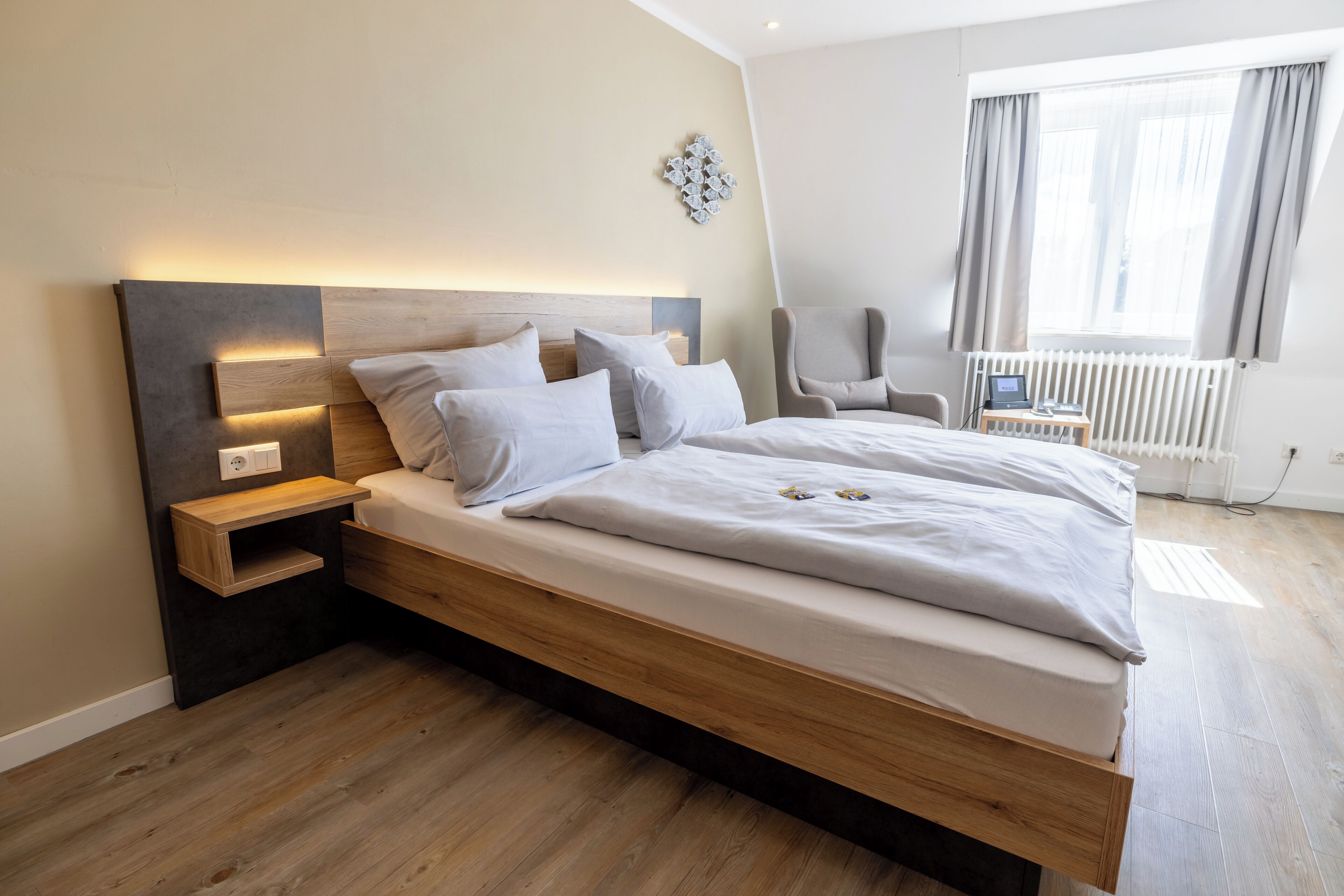 A modern bedroom with a wooden bed, bedside tables, a chair, and a view of the outdoors.