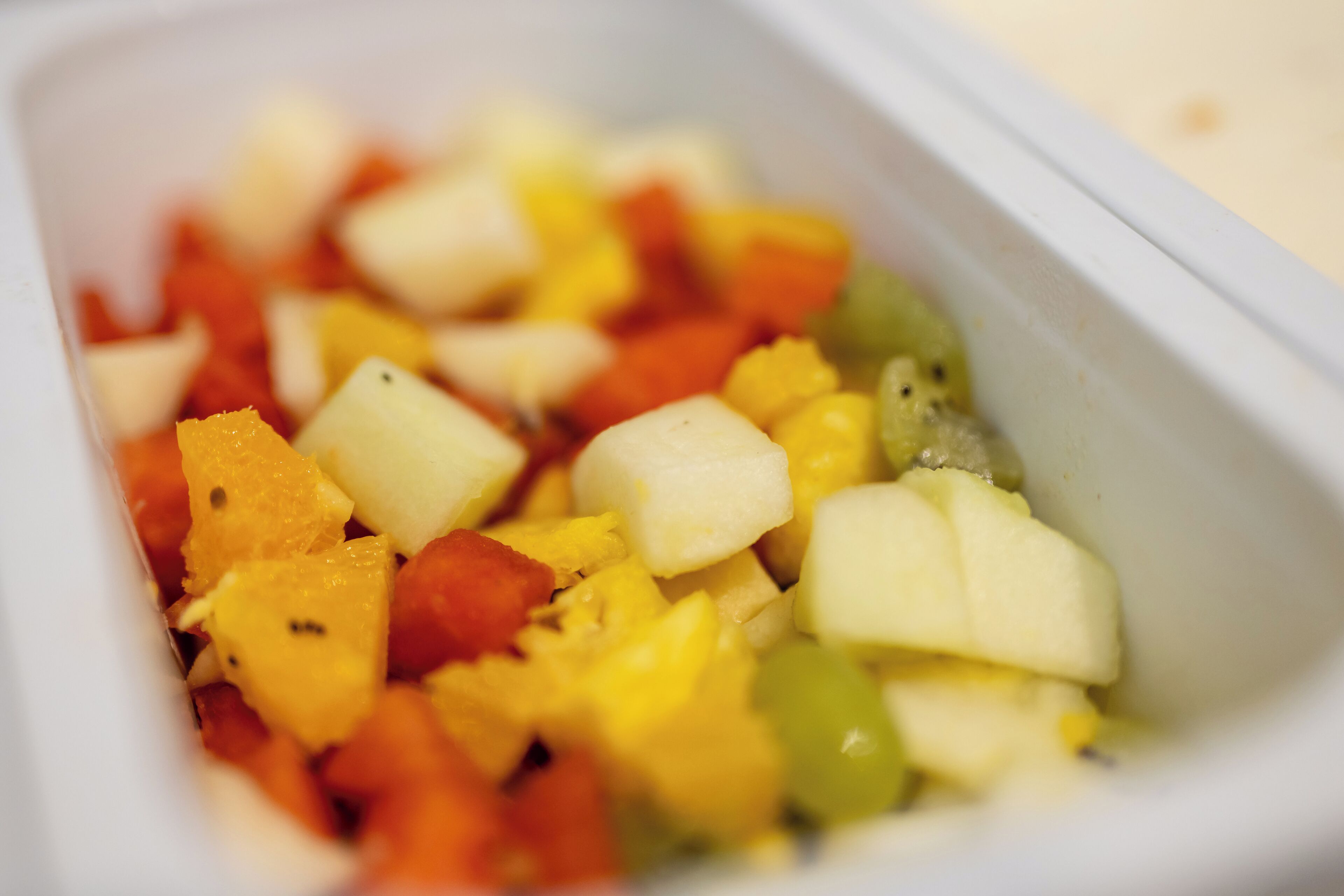 Primer plano de un recipiente con frutas y verduras cortadas en cubos.