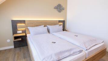 Una cama doble con cabecera de madera y mesitas de noche, un adorno en la pared, y un suelo de tono claro.