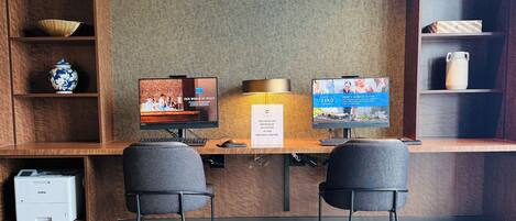 A hotel reception desk with two monitors, a printer, and a computer.