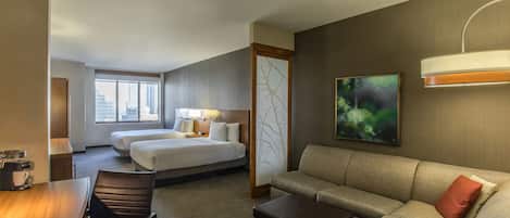Una habitación de hotel con una cama, dos mesitas de noche, un sofá, una mesa de centro y un escritorio.