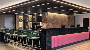 Un espace bar moderne avec un comptoir en marbre noir, des tabourets de bar verts et un mur revêtu de panneaux en bois disposés en motif chevrons.