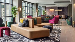 Eine moderne Lobby mit einem beigefarbenen Ecksofa, grünen und roten Sesseln und einem gemusterten Teppich.