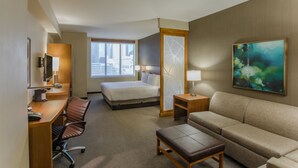 Ein Hotelzimmer mit Bett, Schreibtisch mit Stuhl, Sofa, Fernseher und einem Bild an der Wand.