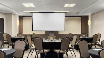 A conference room with a large screen, multiple tables, and chairs arranged for meetings.
