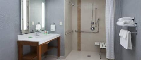 Un baño con tocador de madera, un espejo grande, una ducha con puerta de vidrio y un perchero con toallas dobladas.