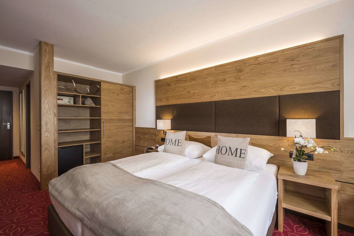 A hotel room with a large bed, wooden headboard, built-in shelving, and a red carpet.