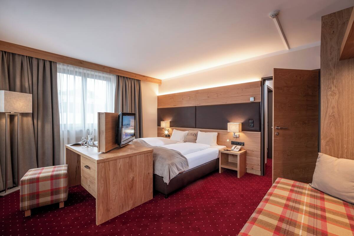 A hotel room with a bed, desk, TV, bedside lamps, and a red carpet.