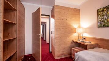 Habitación de hotel con armario de madera, mesita de noche con lámpara, cama y alfombra roja.