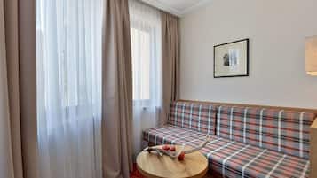 A room with a plaid sofa, a round wooden table with a decorative item, sheer curtains, and a framed picture on the wall.
