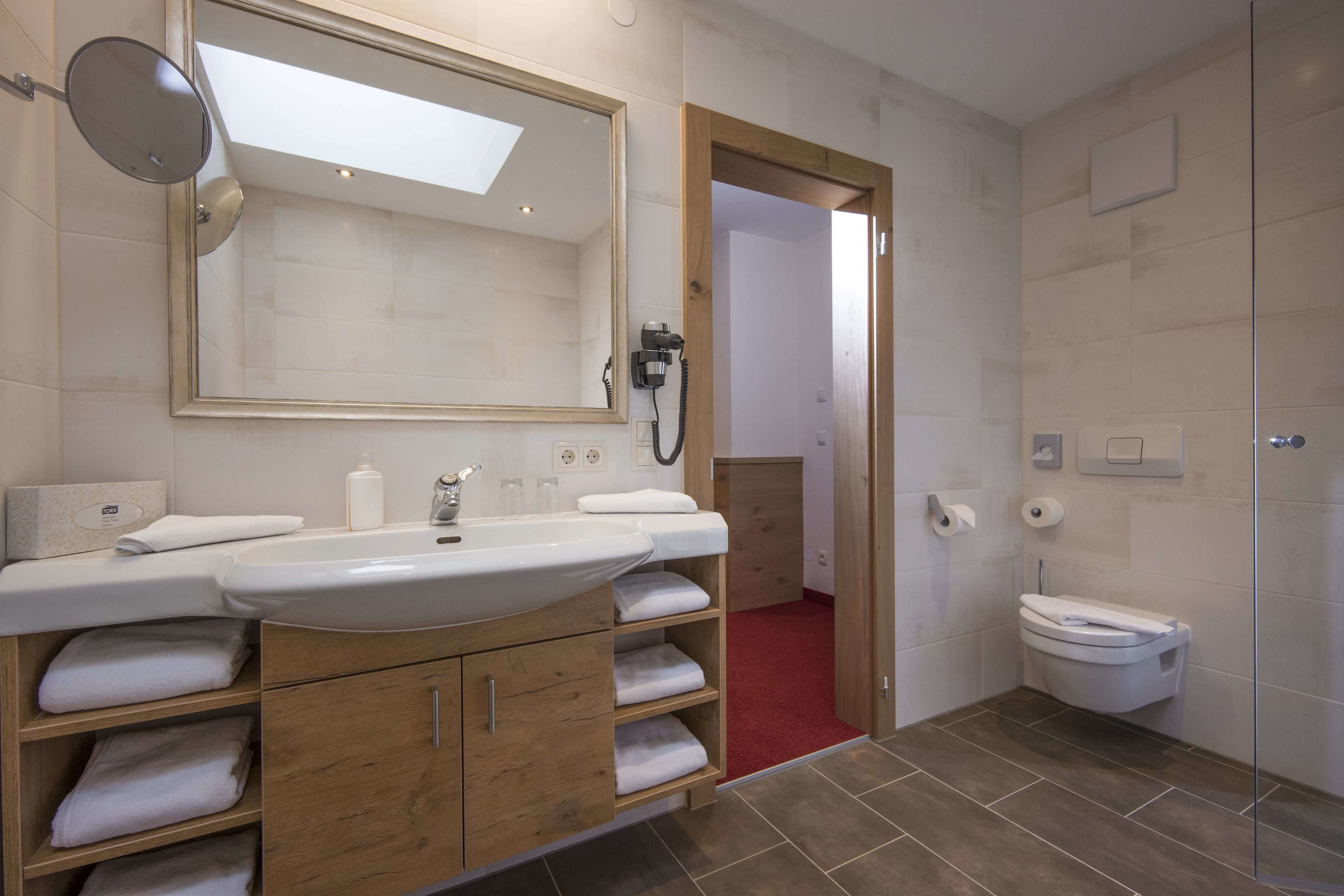 Un baño moderno con un espejo grande, lavamanos dobles, armarios de madera y un inodoro.