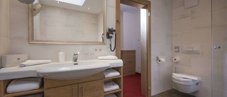 Un baño moderno con un espejo grande, lavamanos dobles, armarios de madera y un inodoro.