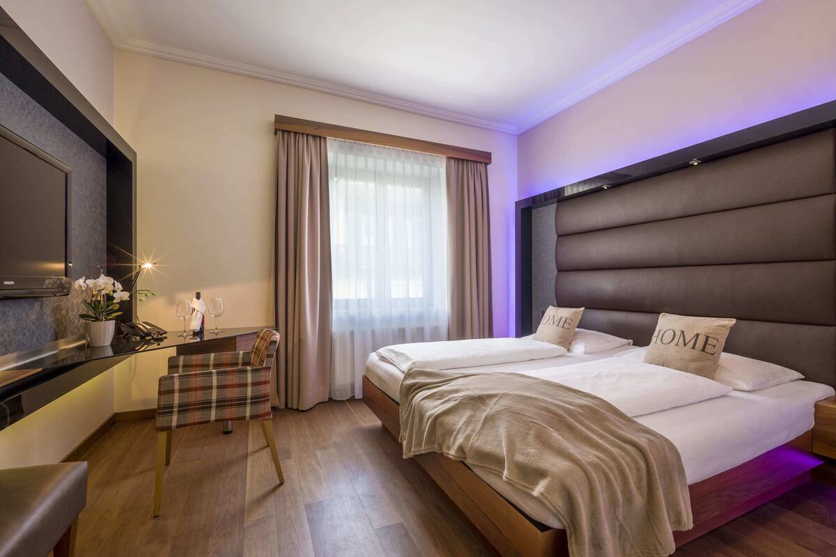 A hotel room with a large bed, a desk with a chair, a TV, and a window with curtains.