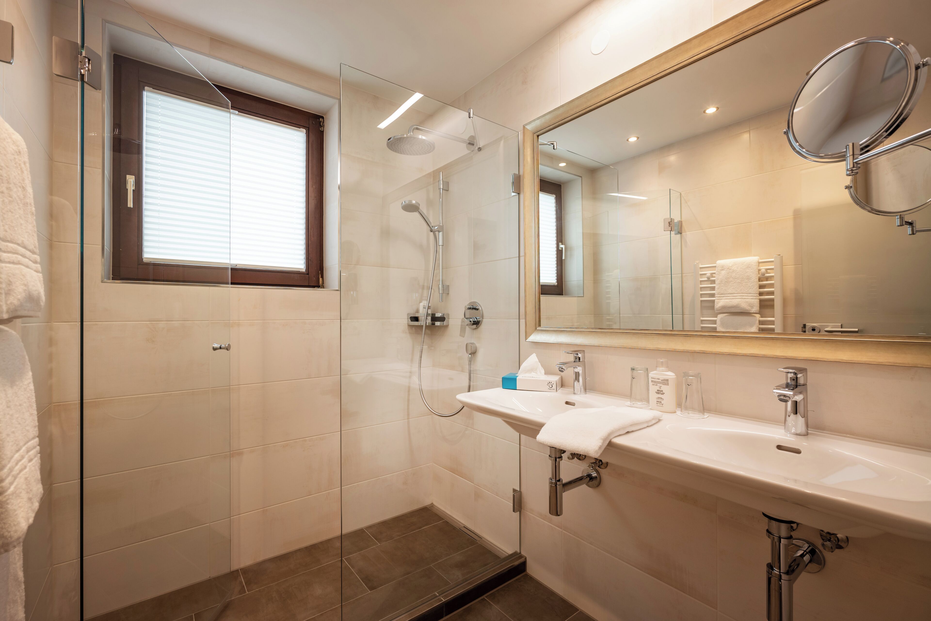 Une salle de bain moderne avec une douche en verre, un lavabo avec un miroir et une fenêtre avec des stores.