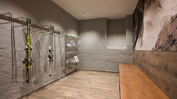 A ski storage area with skis and boots on racks, a wooden bench, and a textured wall.