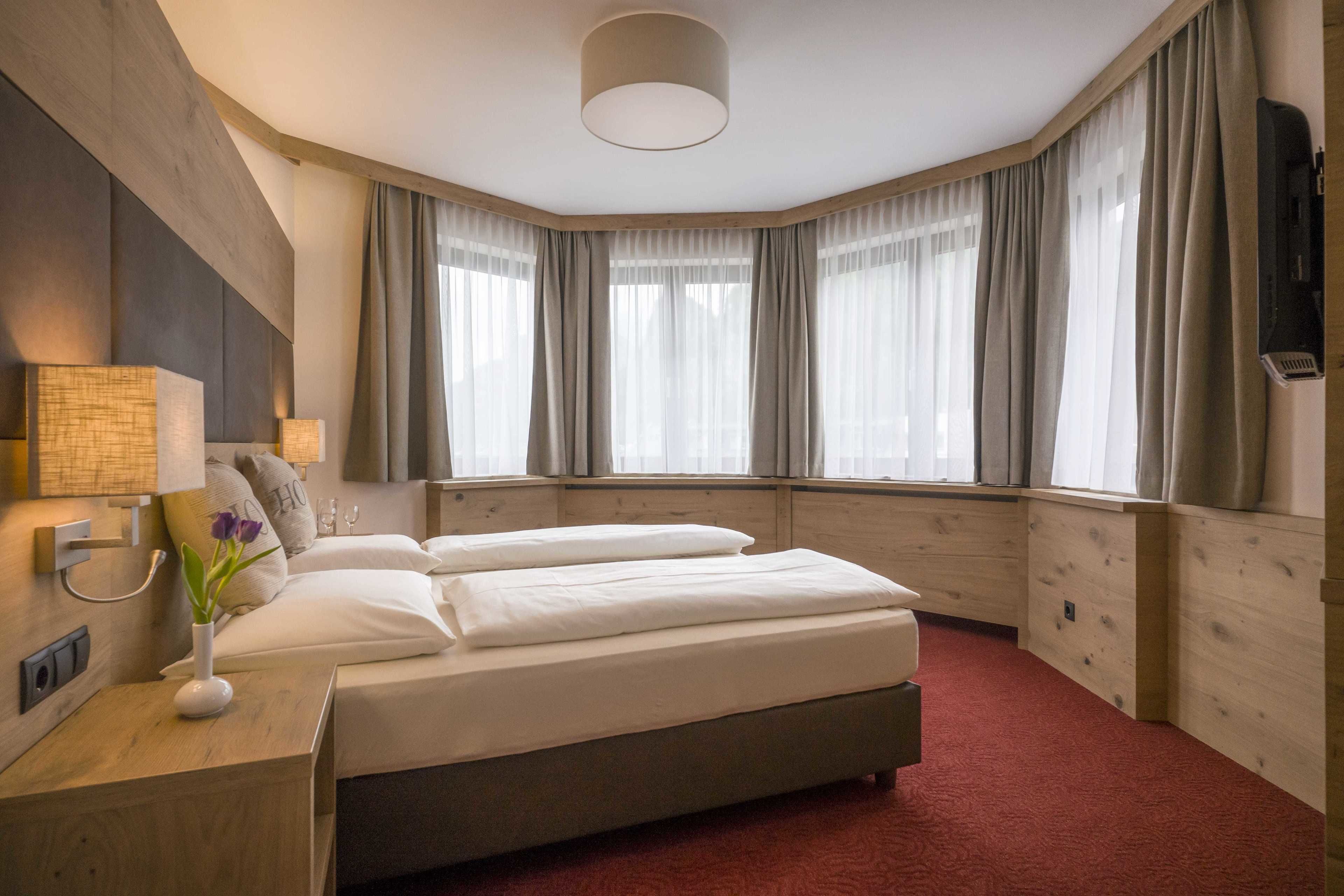 Una habitación de hotel con una cama grande, una mesita de noche con lámpara y una ventana con cortinas.