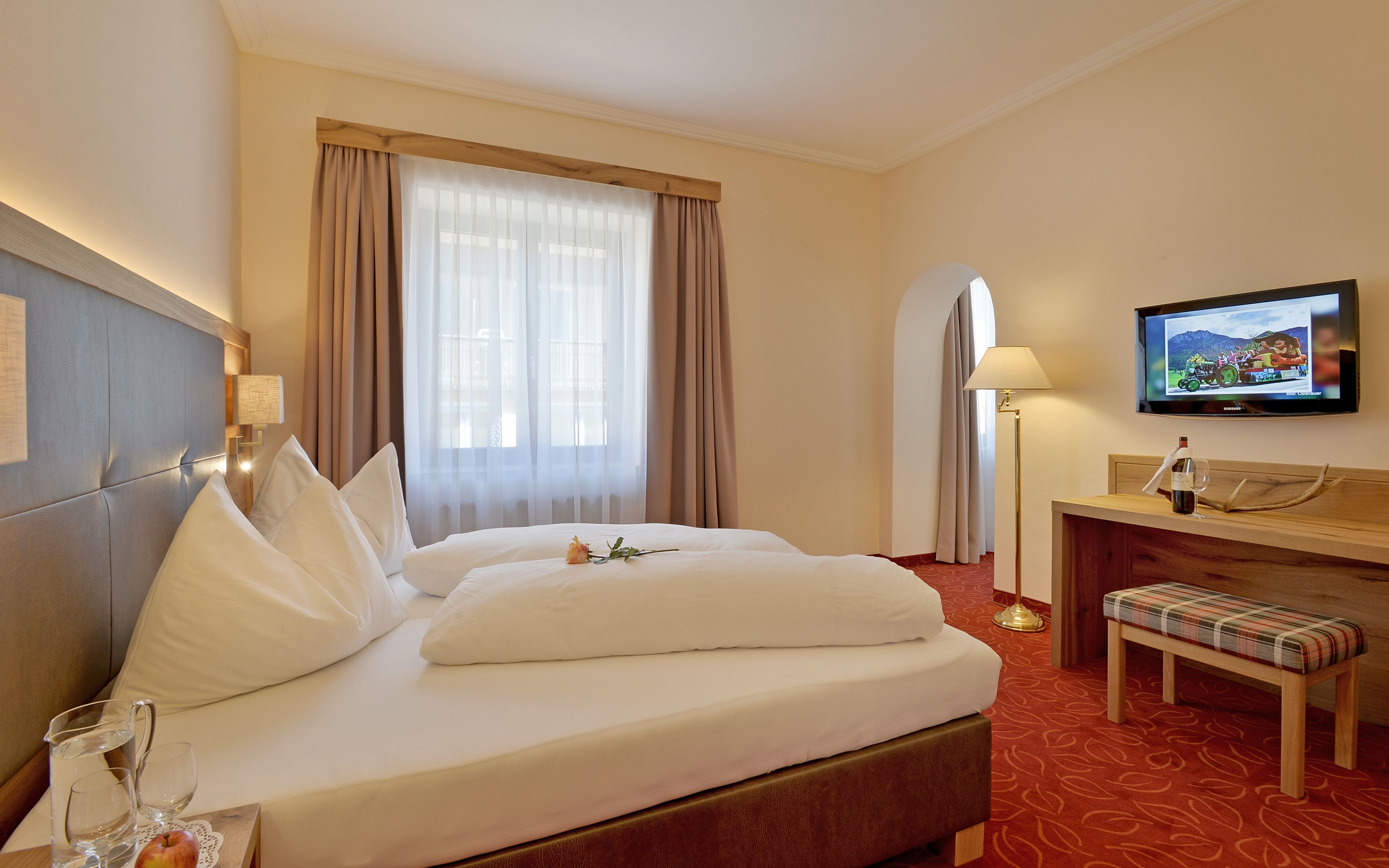 Una habitación de hotel con cama, televisor, escritorio con lámpara y un banco.