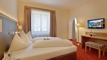 Una habitación de hotel con cama, televisor, escritorio con lámpara y un banco.