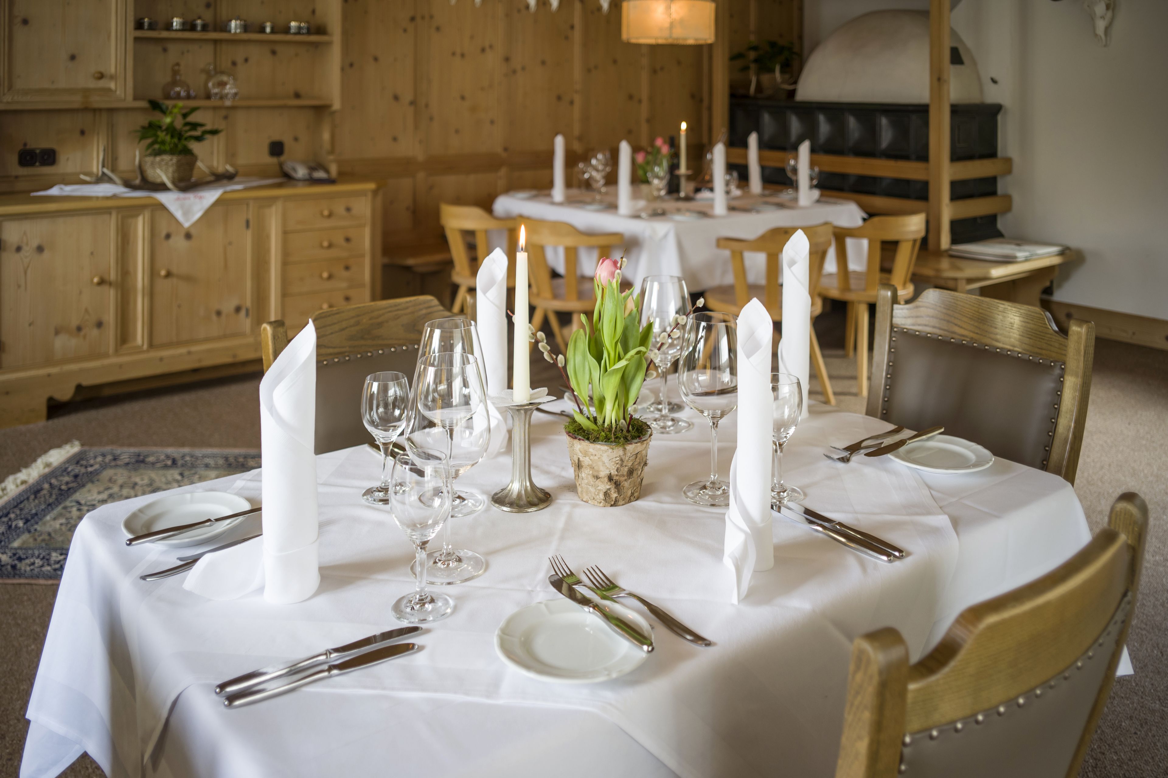 A dining table set with white tablecloth, candles, and a centerpiece of green foliage.