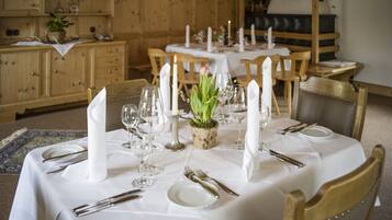 A dining table set with white tablecloth, candles, and a centerpiece of green foliage.