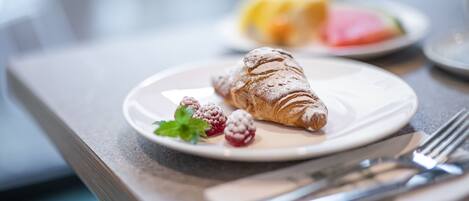 A croissant on a plate with raspberries and mint, a fork, and a knife on a table.