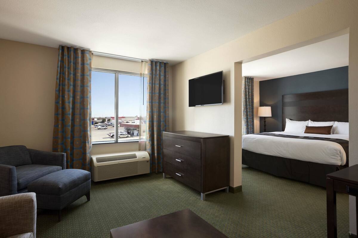 A hotel room with a bed, a TV, a desk, a chair, a dresser, and a window with curtains.
