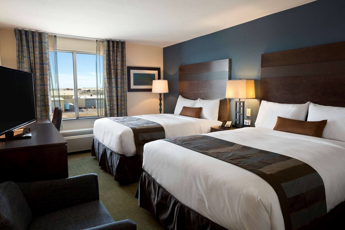 A hotel room with two beds, a TV, a desk, and a view of the city.