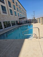 Una piscina con letrero de prohibición de clavados, rodeada de sillas de descanso y un edificio con múltiples ventanas.
