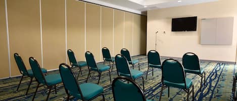 Un salón de conferencias con filas de sillas color turquesa, un televisor de pantalla plana y una pizarra en la pared.