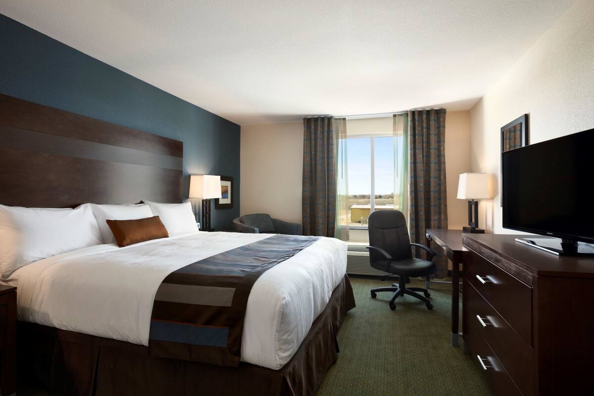 A hotel room with a large bed, a desk with a television, a chair, and a window with curtains.