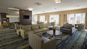 Un hall d’hôtel avec un canapé, des fauteuils, une table basse et un téléviseur fixé au mur.