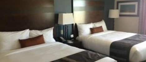 A hotel room with two beds, dark headboards, white bedding, and a nightstand with a lamp.