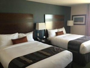 A hotel room with two beds, dark headboards, white bedding, and a nightstand with a lamp. - Wingate By Wyndham Seminole (Seminole)