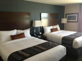 Una habitación de hotel con dos camas, cabeceros oscuros, ropa de cama blanca y una mesita de noche con lámpara.