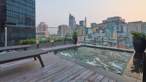 A rooftop pool with wooden decking and seating, surrounded by city buildings and potted plants. - Cherry Boutique Hotel (Ho Chi Minh City)