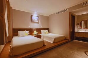 A hotel room with two beds, a wooden headboard, a bedside table with a lamp, a framed picture on the wall, and a bathroom with a mirror and sink. - Cherry Boutique Hotel (Ho Chi Minh City)