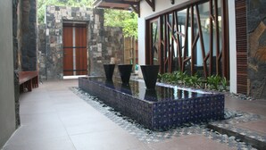A modern building with a stone wall, a wooden door, and a tiled water feature. - Dodola Lodge (Grand-Baie)