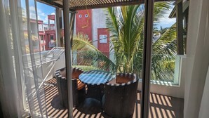 A balcony with wicker furniture and a view of palm trees and buildings. - Dodola Lodge (Grand-Baie)