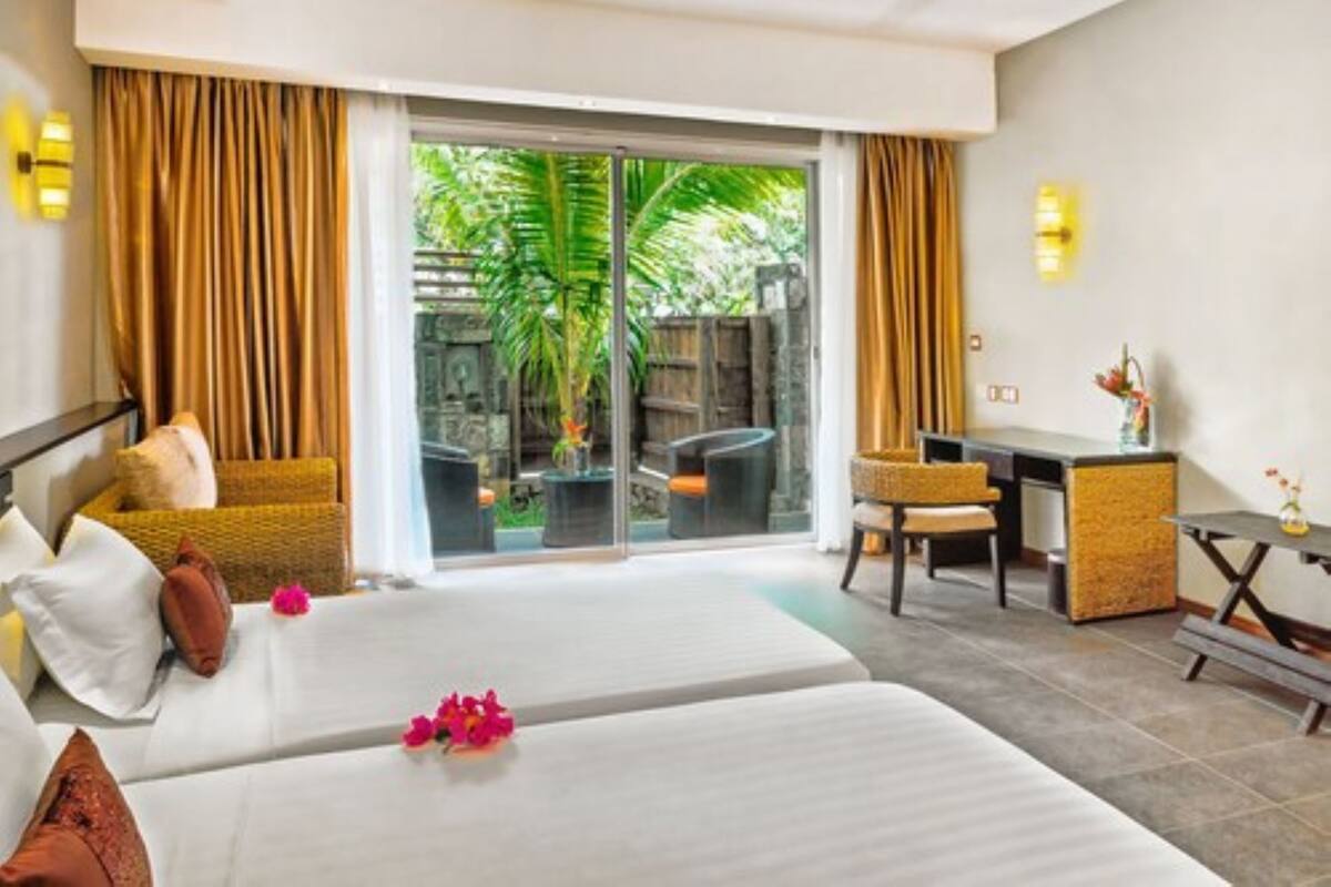 Une chambre d’hôtel avec deux lits, un bureau et un coin salon donnant sur un espace verdoyant.