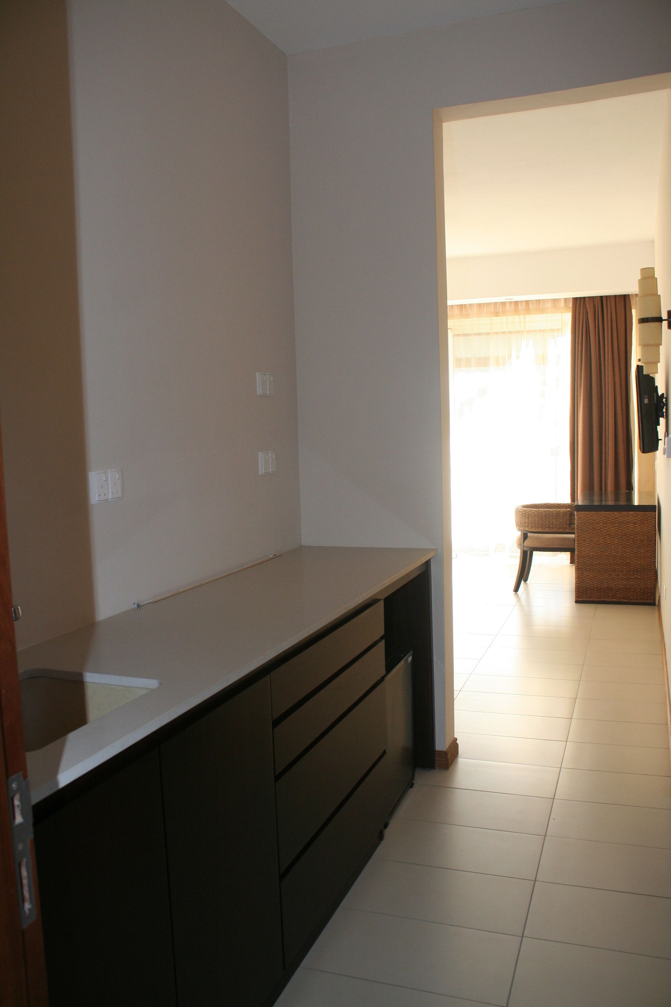 A modern kitchen with dark cabinetry, a countertop, and a view into a dining area with a chair and table.