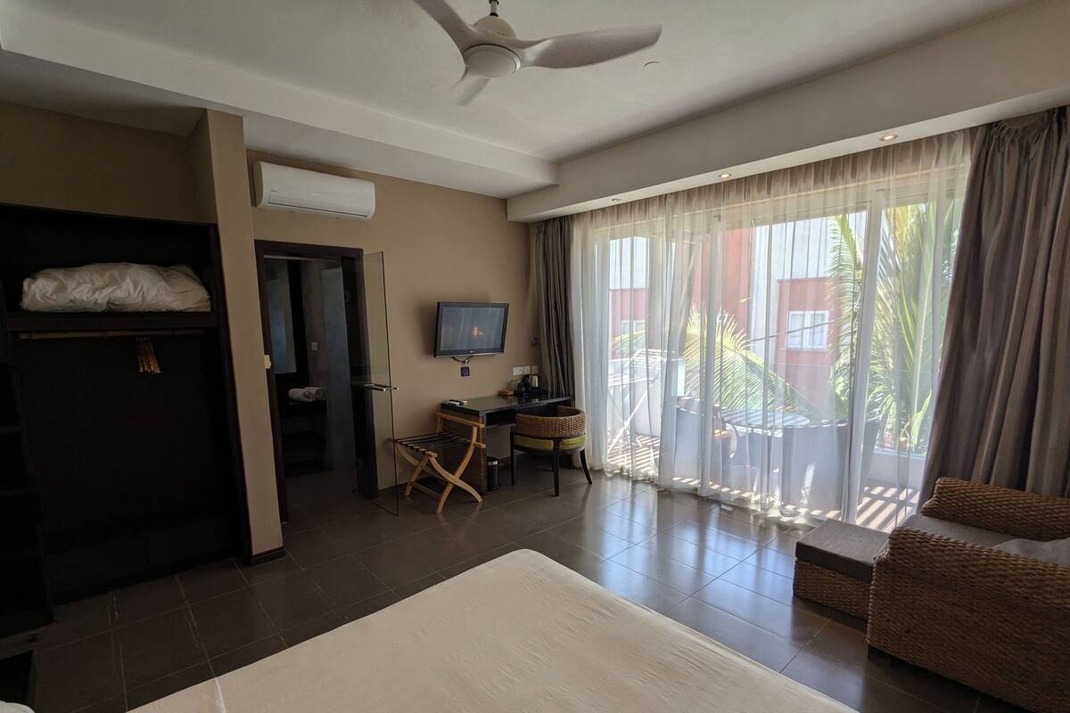 Une chambre d’hôtel avec un lit, un bureau, une télévision et un balcon avec des rideaux.