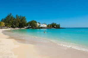 Una playa con agua turquesa cristalina, una orilla arenosa y un edificio de fachada blanca.