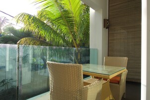 Un balcón con barandilla de vidrio, sillas de mimbre, una mesa de cristal y una palmera.