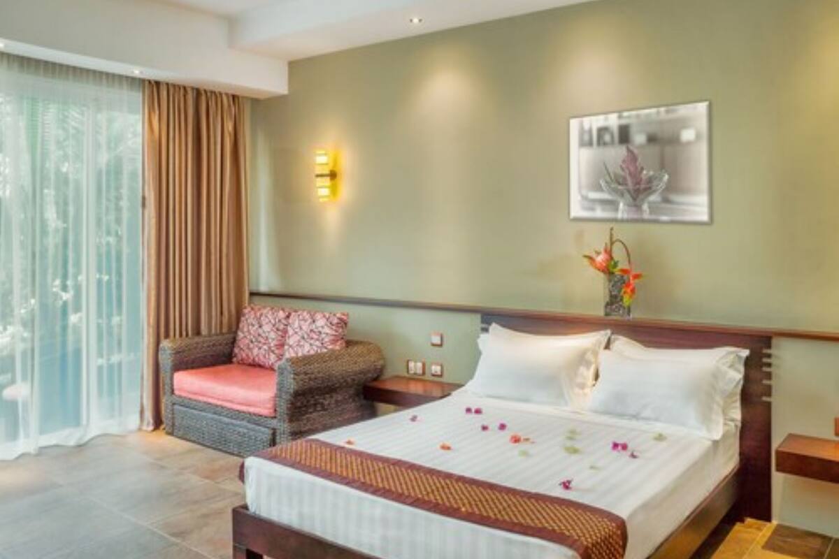 Une chambre d’hôtel avec un lit, une chaise, une table de chevet et une lampe fixée au mur.