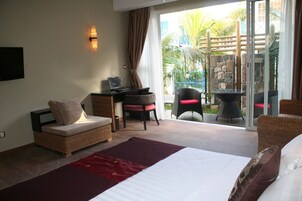Habitación de hotel con cama, escritorio con computadora portátil, silla de mimbre y mesa de comedor con sillas.