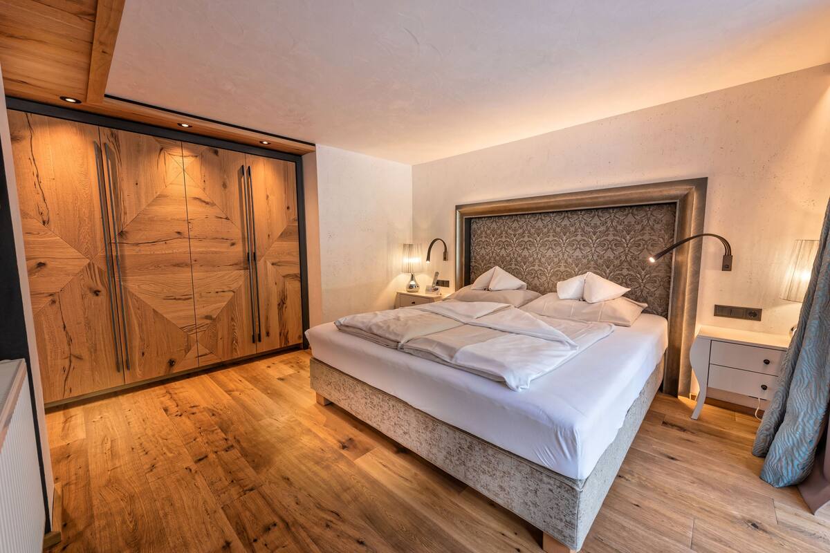 A bedroom with a large bed, wooden wardrobe, and bedside lamps.