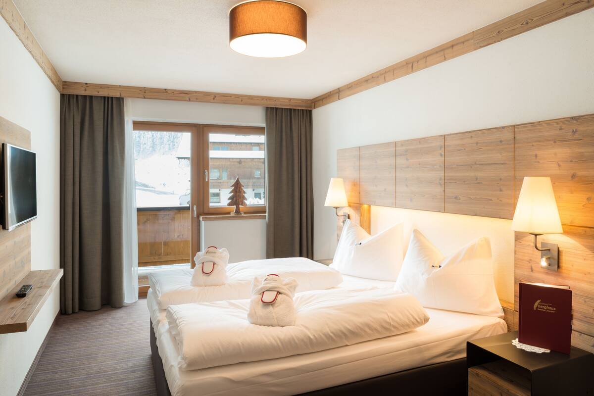 A hotel room with a large bed, two bedside lamps, a TV on a shelf, and a view of a snowy landscape through the window.
