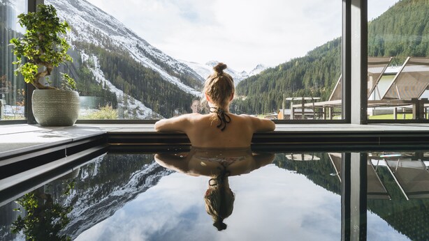 Una persona relajándose en un baño de spa con vista a montañas nevadas y un bosque.